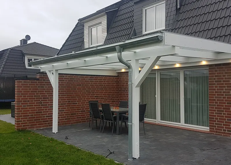 Weiß lackiertes Holz-Terrassendach mit Glaseindeckung und LED-Spots an einem Klinkerhaus, darunter Esstisch